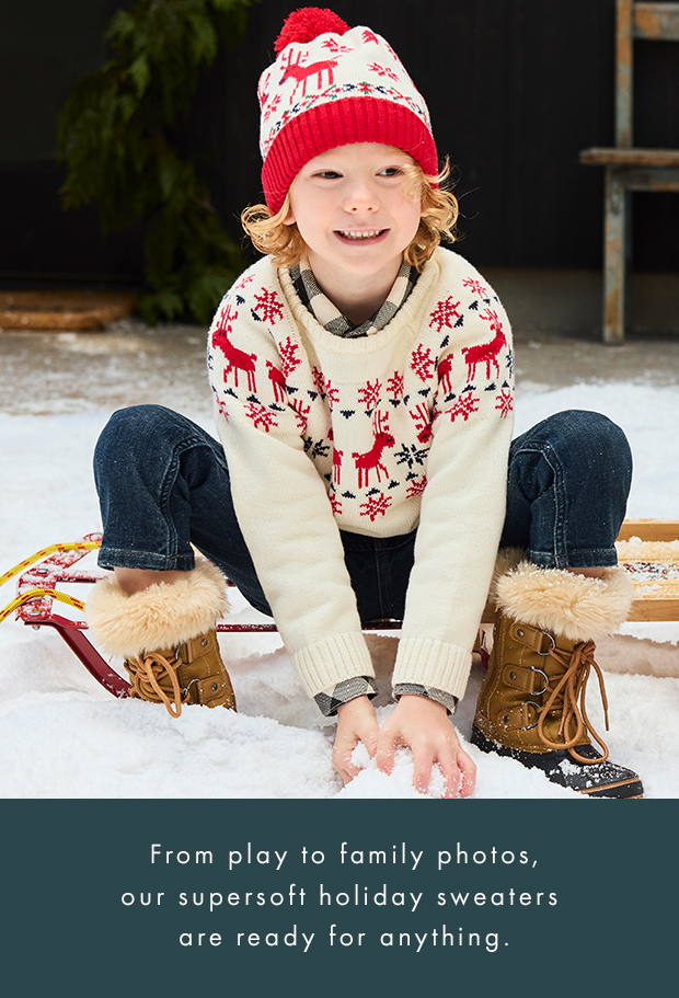 a boy making a snowball wearing deer print sweater and beanie